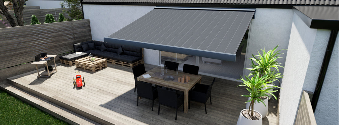 Grårandig markis över en uteplats av trall, huset har en vit putsad fasad. På uteplatsen står en grill, en soffgrupp byggd av EU-pallar, en matgrupp står i skuggan av markisen.