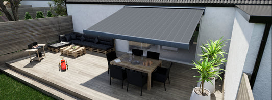 Grårandig markis över en uteplats av trall, huset har en vit putsad fasad. På uteplatsen står en grill, en soffgrupp byggd av EU-pallar, en matgrupp står i skuggan av markisen.