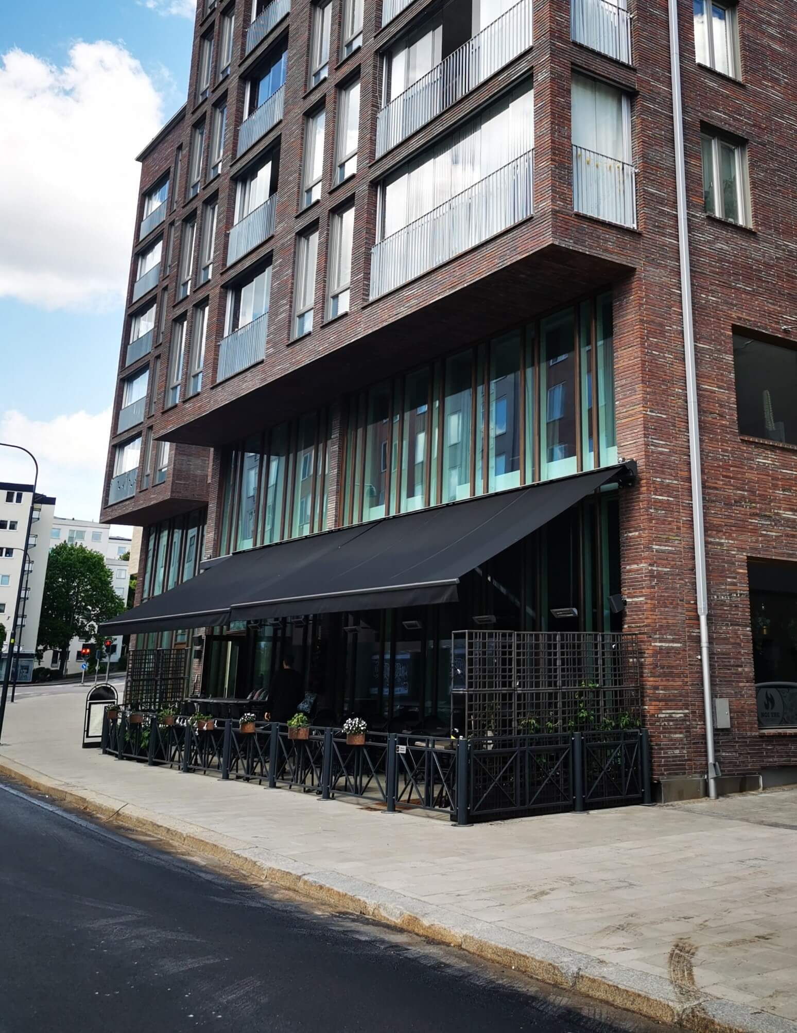 Jamaica inkl skyddshuv i Antracit - FSM71319 samt svart markisväv monterad över restaurangens uteservering. Elektrisk styrning inklusive skaksensor som tillval för att markisen skall stängas när vinden börjar blåsa.