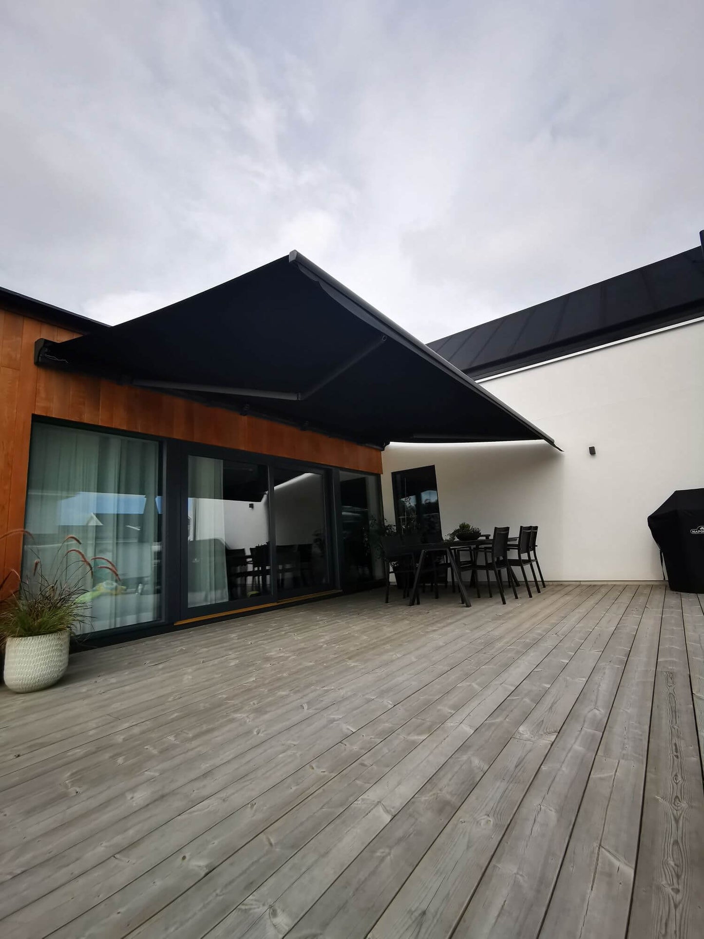 Jamaica inkl skyddshuv i Antracit - FSM71319 samt svart markisväv monterad över uteplatsen med tralldäck. Elektrisk styrning inklusive skaksensor som tillval för att markisen skall stängas när vinden börjar blåsa.