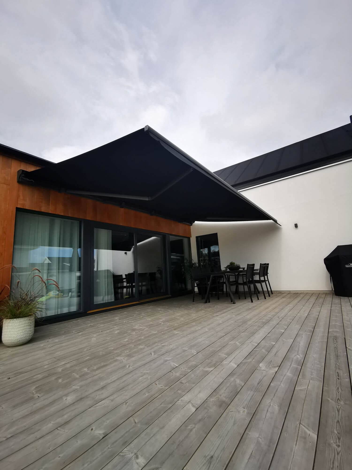 Jamaica inkl skyddshuv i Antracit - FSM71319 samt svart markisväv monterad över uteplatsen med tralldäck. Elektrisk styrning inklusive skaksensor som tillval för att markisen skall stängas när vinden börjar blåsa.