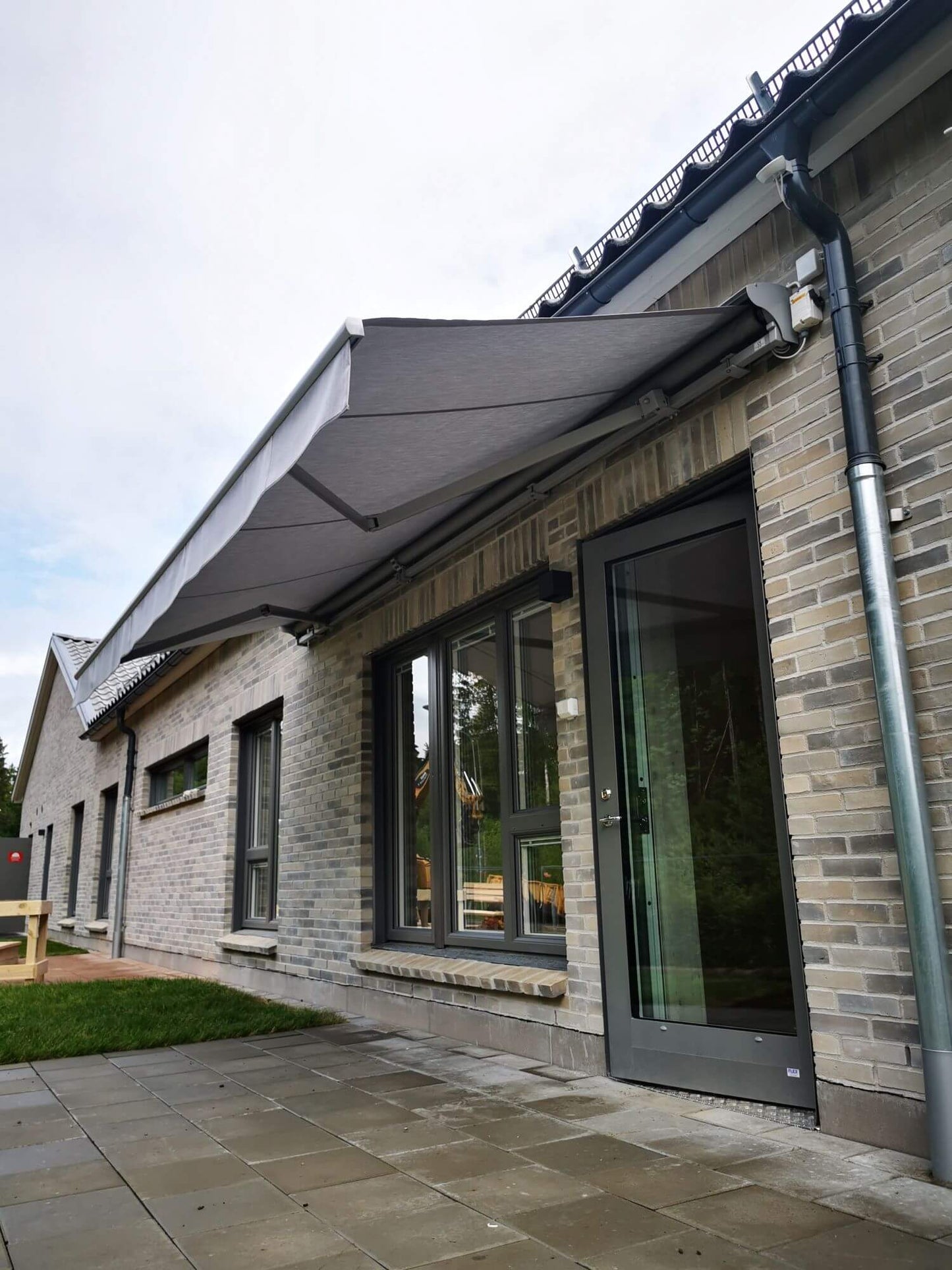 Jamaica inkl skyddshuv i grå kulör RAL9006 med ljusgrå markisväv monterad över uteplatsen. Elektrisk styrning.