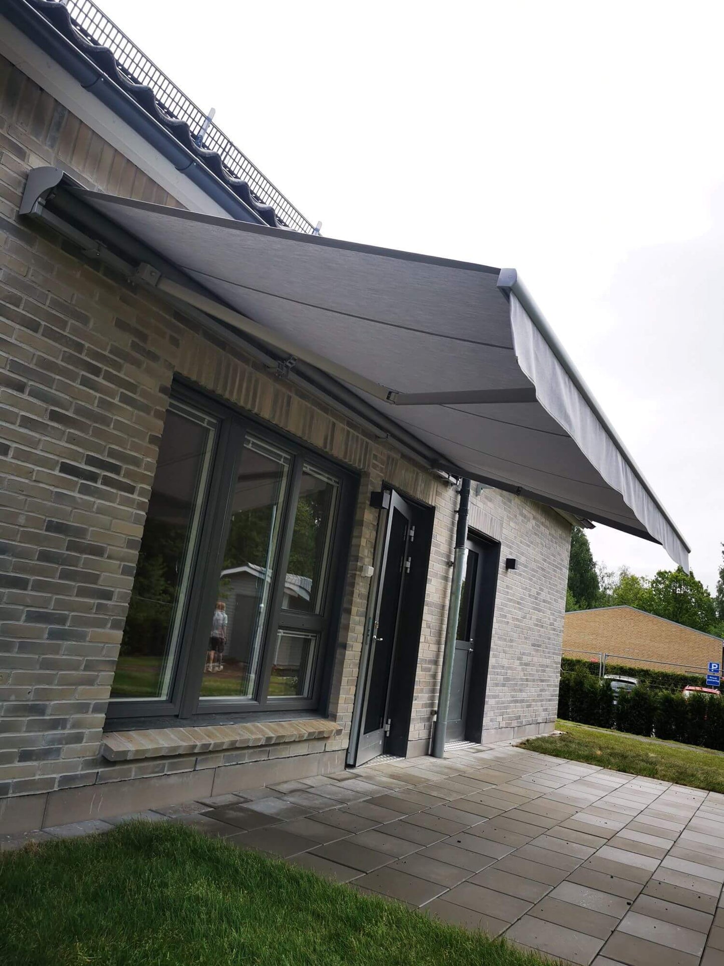 Jamaica inkl skyddshuv i grå kulör RAL9006 med ljusgrå markisväv monterad över uteplatsen. Elektrisk styrning.