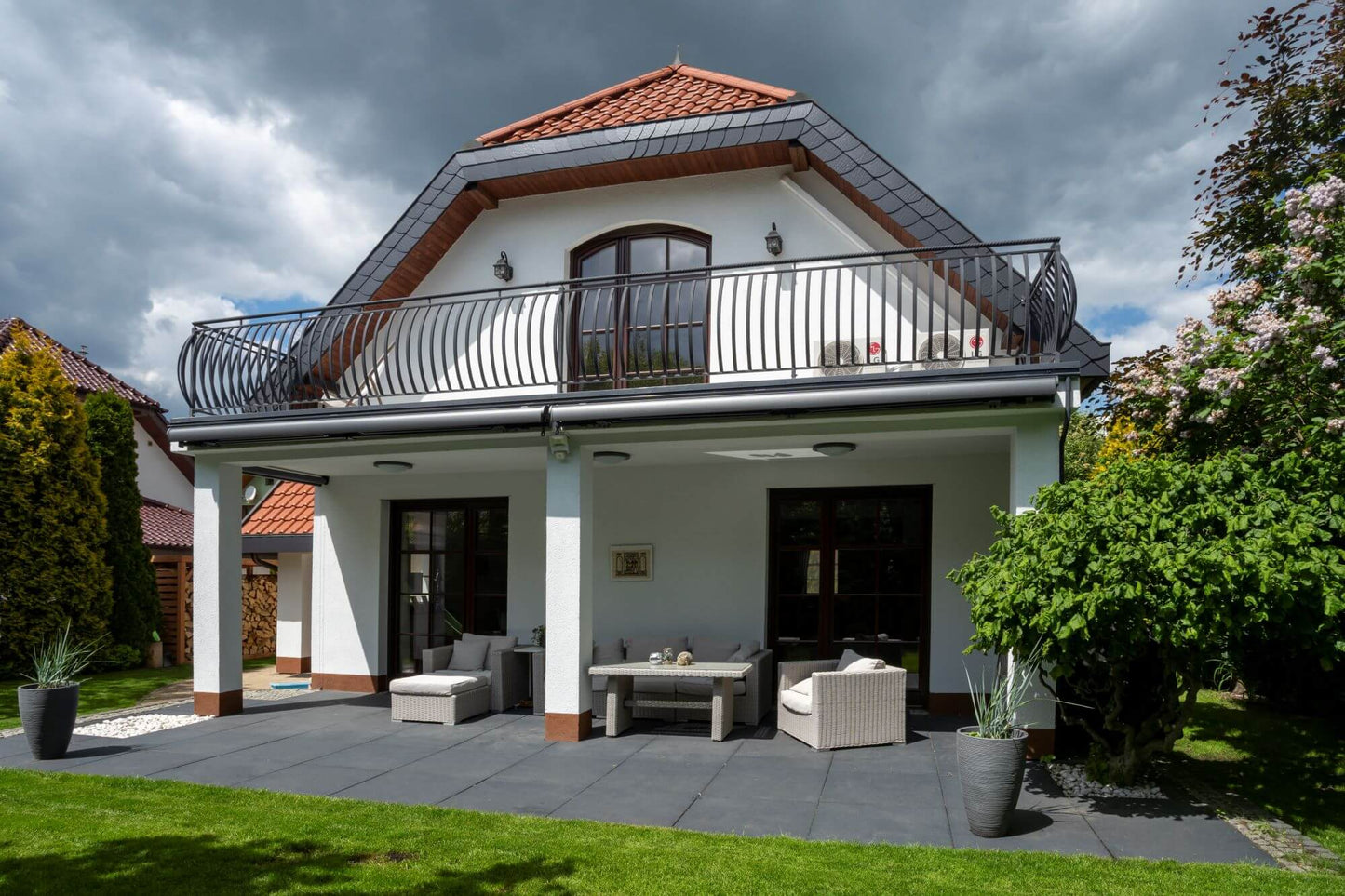 Robust, kvalitativ, grå terrassmarkis, markisen har grå silver RAL9006 konstruktion med ljusgrå markisväv. Monterad på en uteplats med stenplattor och gräsmatta. Premium Markis, modell Palladio. premium-markis.se