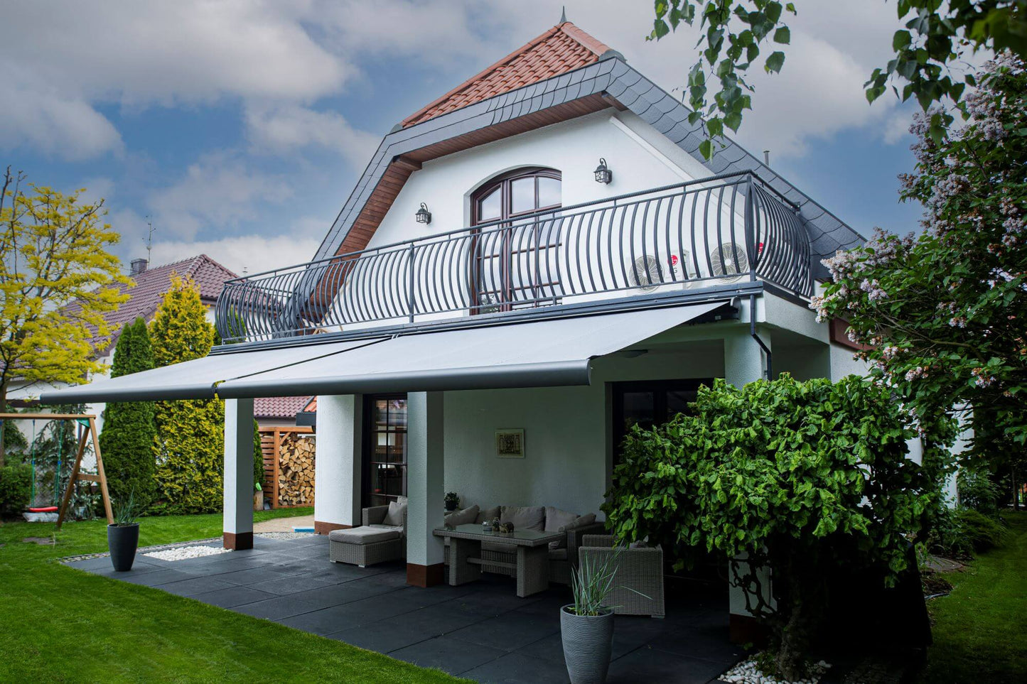Robust, kvalitativ, grå terrassmarkis, markisen har grå silver RAL9006 konstruktion med ljusgrå markisväv. Monterad på en uteplats med stenplattor och gräsmatta. Premium Markis, modell Palladio. premium-markis.se