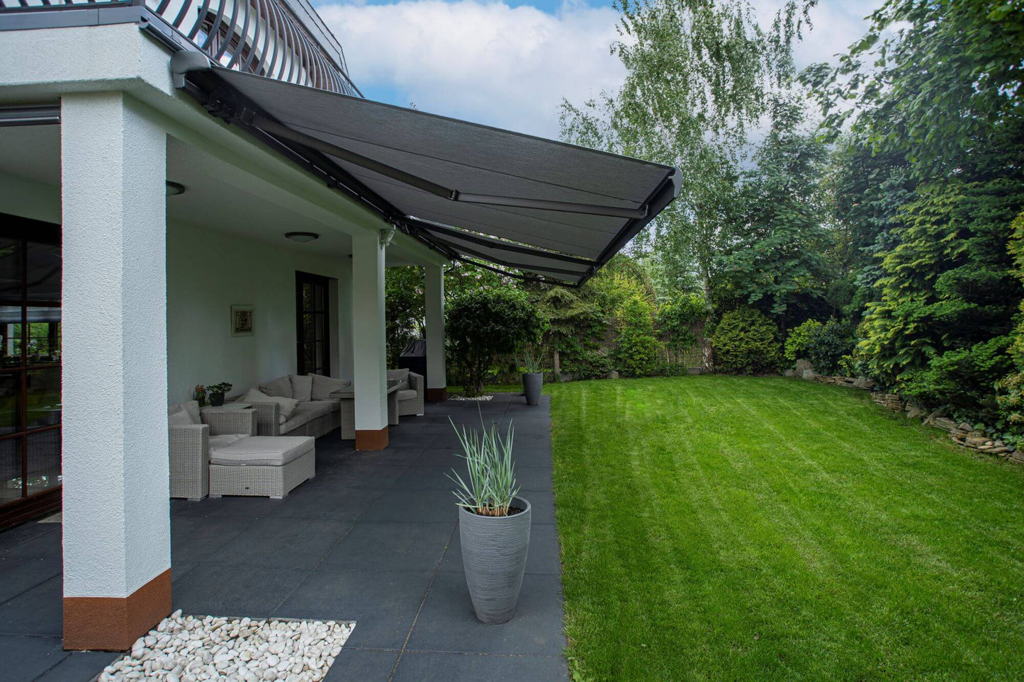 Robust, kvalitativ, grå terrassmarkis, markisen har grå silver RAL9006 konstruktion med ljusgrå markisväv. Monterad på en uteplats med stenplattor och gräsmatta. Premium Markis, modell Palladio. premium-markis.se