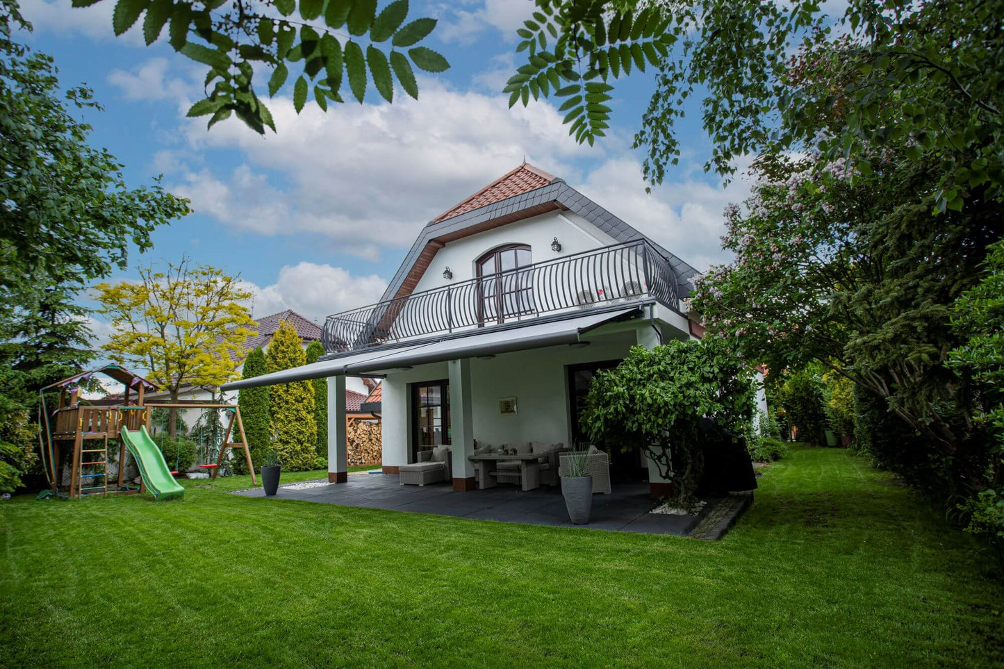 Robust, kvalitativ, grå terrassmarkis, markisen har grå silver RAL9006 konstruktion med ljusgrå markisväv. Monterad på en uteplats med stenplattor och gräsmatta. Premium Markis, modell Palladio. premium-markis.se