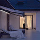 Modern terrassmarkis med integrerad LED-belysning på en uteplats vid skymning, markisen har svart konstruktion med ljus markisväv. Premium Markis, modell Corsica. premium-markis.se