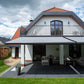 Robust, kvalitativ, grå terrassmarkis, markisen har grå silver RAL9006 konstruktion med ljusgrå markisväv. Monterad på en uteplats med stenplattor och gräsmatta. Premium Markis, modell Palladio. premium-markis.se